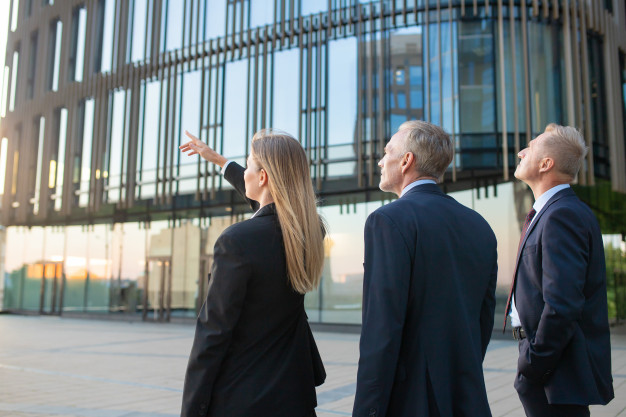 agent-customers-meeting-outdoors-discussing-real-property-pointing-office-building-back-view-commercial-real-estate-concept_74855-6738