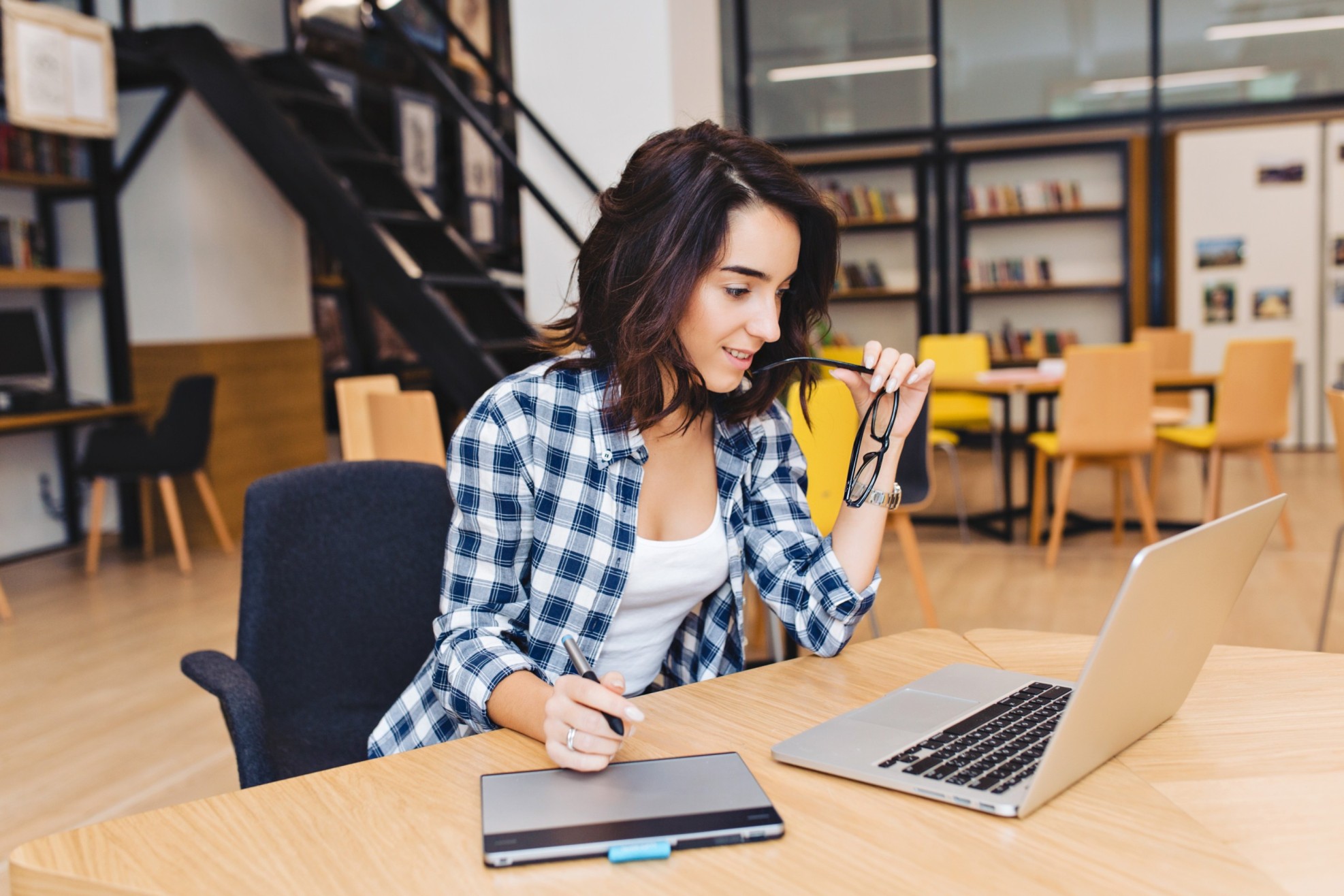 pretty-brunette-young-woman-studying-with-laptop-library-clever-student-university-life-surfing-internet-busy-working-expressing-positive-emotions-smiling-playing-with-black-glasses (1) (1) (1)