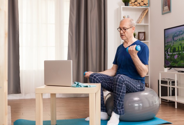 senior-man-training-with-online-coach-sitting-swiss-ball-middle-room_482257-119