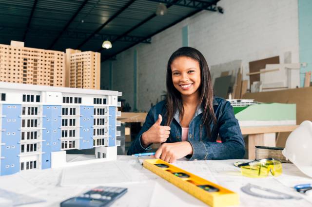 smiling-african-american-woman-showing-thumb-up-near-model-building (1)