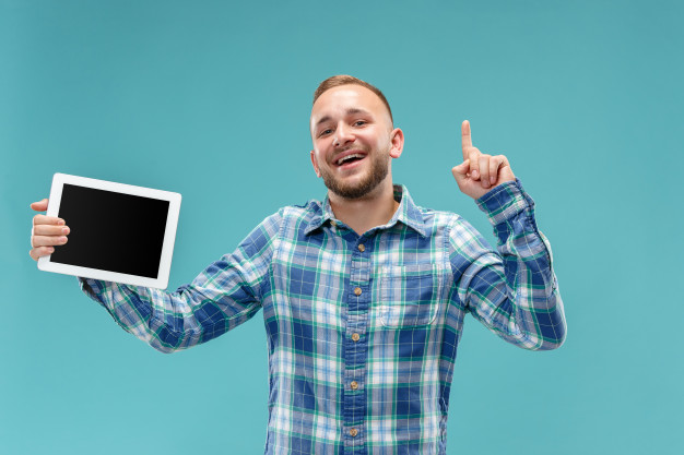 studio-picture-positive-man-isolated-blue-wall-standing-casual-clothes-holding-tablet-showing-it-blank-screen-with-happy-smile_155003-9340