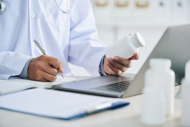 unrecognizable-female-doctor-with-laptop-holding-medication-writing-prescription_1098-17464