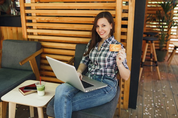 woman-outdoors-street-summer-coffee-shop-wooden-cafe-sitting-working-laptop-pc-computer-hold-bank-credit-card-relaxing-during-free-time_365776-3941