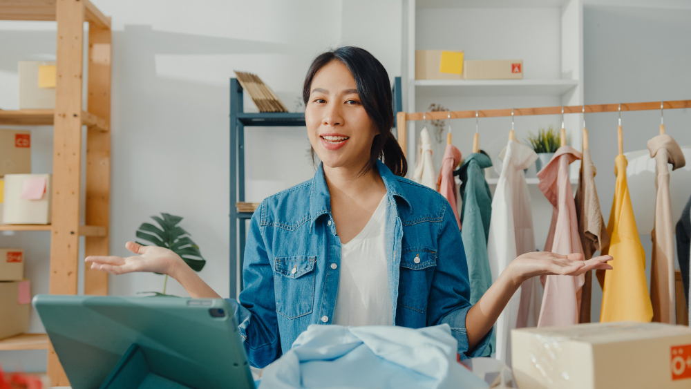 young-asian-lady-fashion-designer-using-mobile-phone-receiving-purchase-order-show-clothes-live-streaming